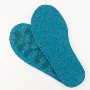 A pair of Joe's Toes Adult's Thick Felt Slipper Soles w/Latex Grip is placed on a white surface. One sole is tilted and slightly overlapping the other, revealing visible wear with darker spots on the left sole. The eco-friendly wool texture of the felt is clearly visible.