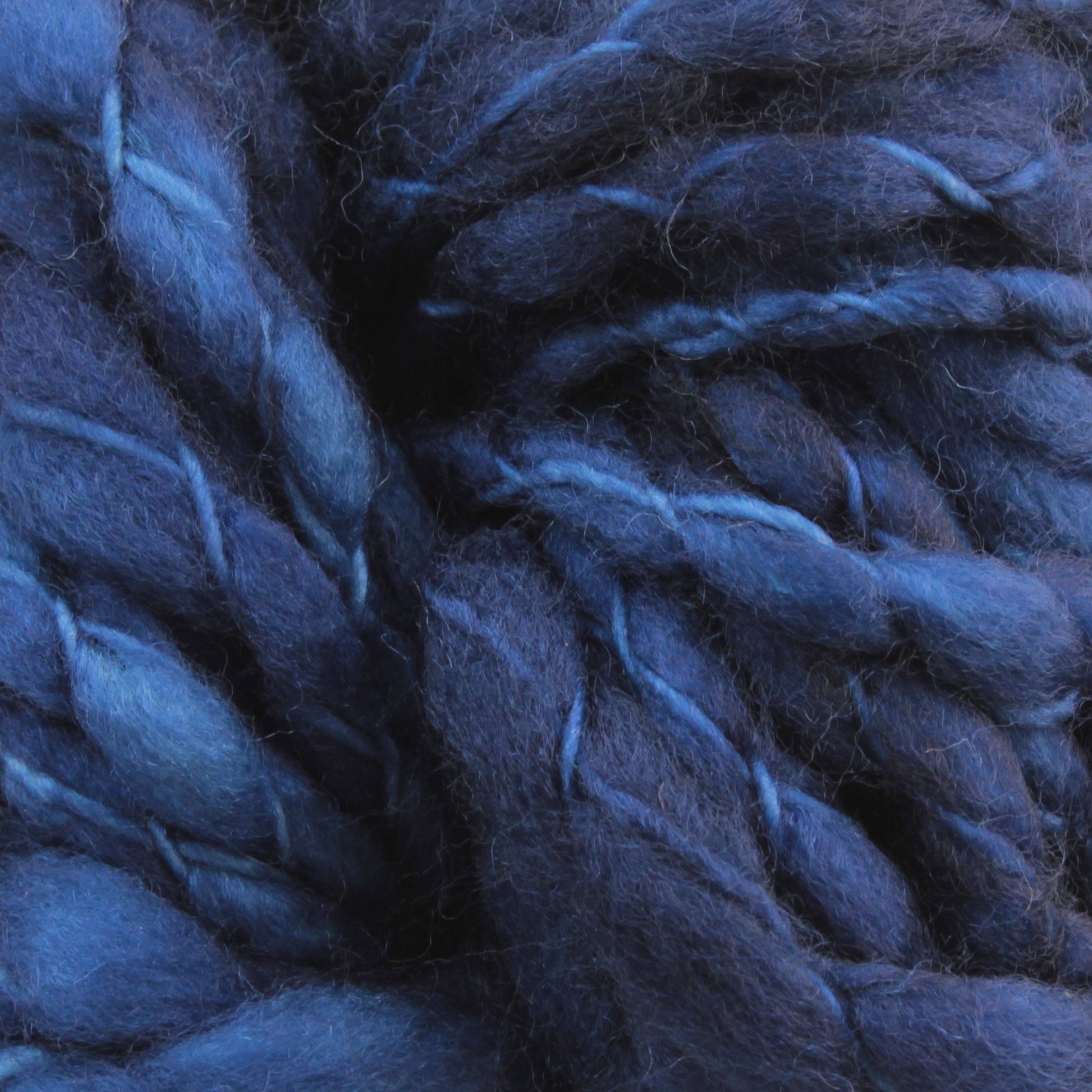 Close-up of dense, intertwined blue and indigo yarn fibers, showcasing various shades and textures. The super bulky Malabrigo Caracol appears soft and fluffy, forming a rich tapestry of dark and light blue hues. This kettle-dyed superwash merino wool from Malabrigo Yarn promises both warmth and luxurious comfort.