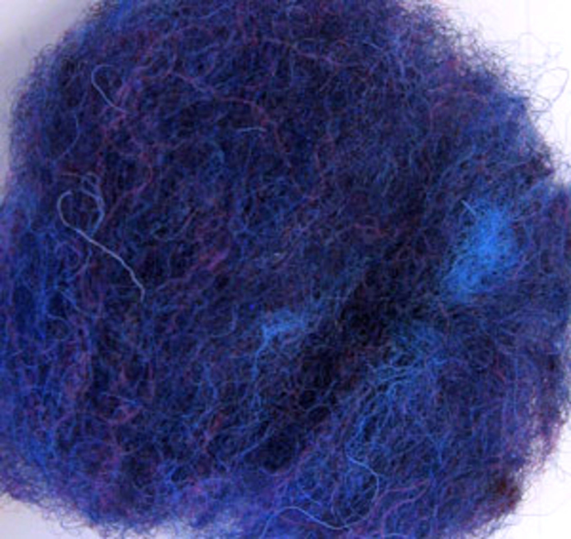 A close-up image of a tangled ball of dark blue Harrisville Dyed & Carded Wool Fiber from Harrisville Designs. The fibers are matted together, creating a dense and fuzzy texture with some lighter blue and heathered colors visible throughout. The background is slightly blurred, directing attention to the wool.