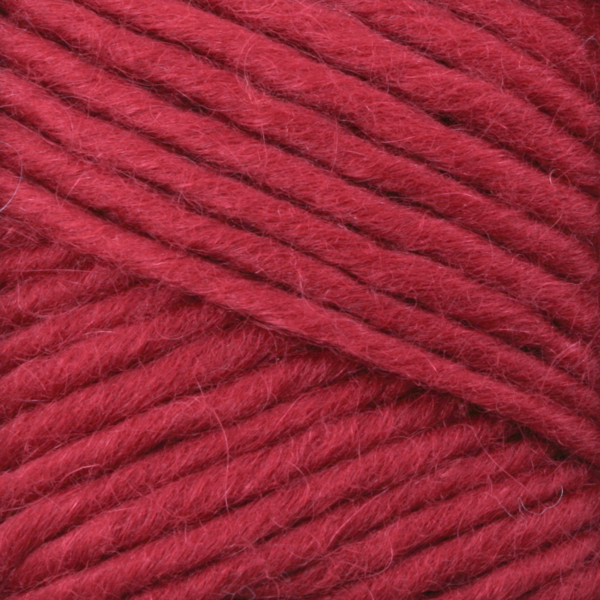 Close-up image of thick, red Lamb's Pride Worsted Yarn strands, neatly wound and displaying a soft, slightly fuzzy texture. The yarn appears rich in color, suggesting warmth and a cozy feel, perfect for Navajo style weaving or felting projects to create warm garments or accessories by Brown Sheep.