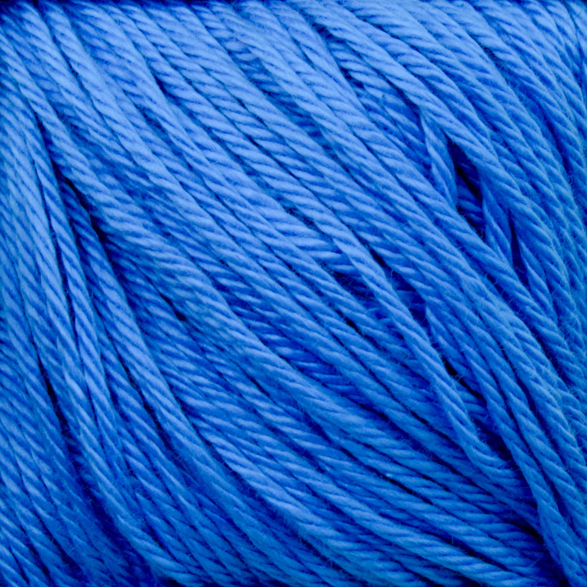 A close-up image of Cascade Ultra Pima Cotton Yarn by Cascade Yarns, showing tightly wound strands creating a textured pattern. The yarn appears soft and is neatly coiled, highlighting its rich blue color and fine quality. This yarn's soft hand speaks to its luxurious Peruvian Pima Cotton origins.