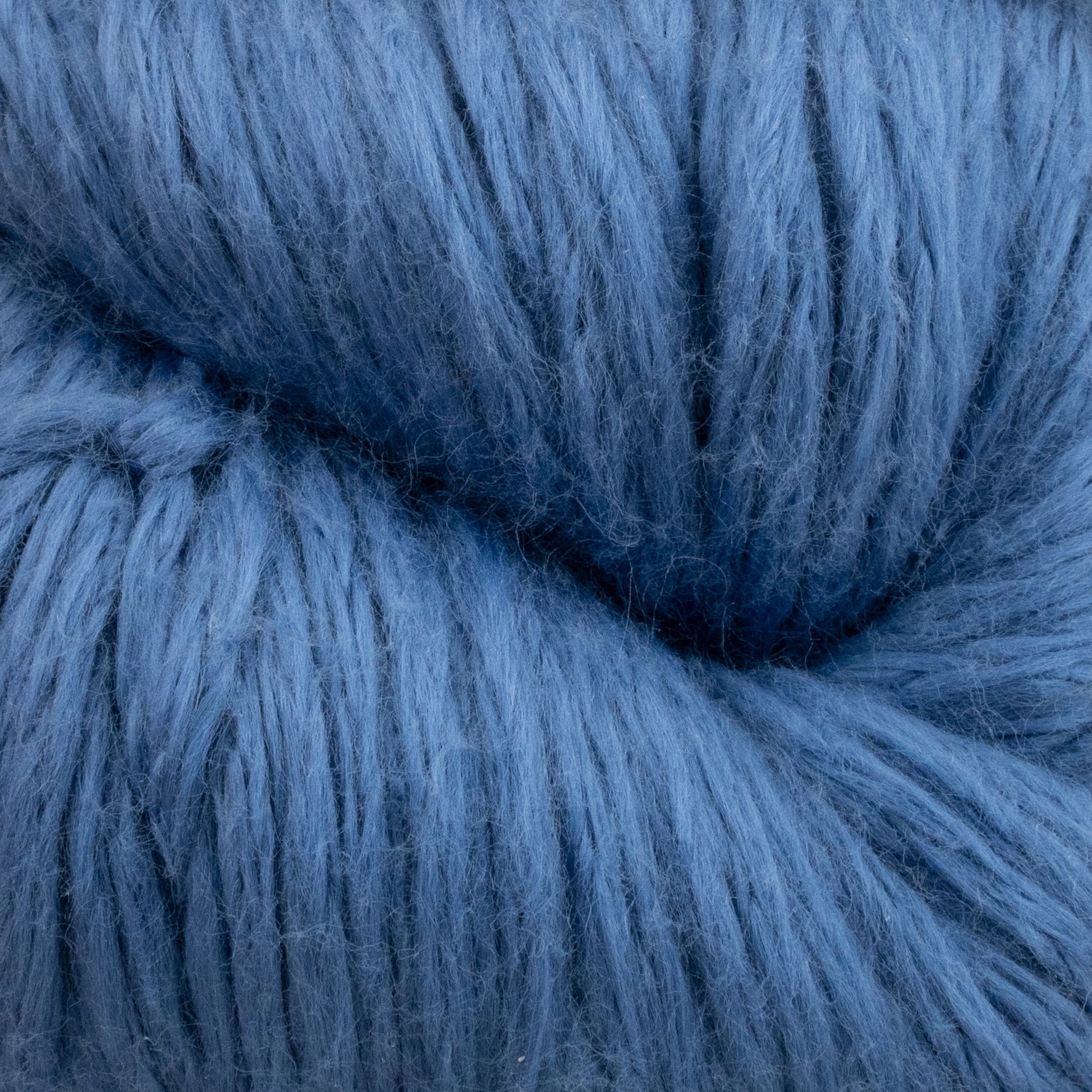 Close-up of a skein of Cumulus Cotton by Juniper Moon Farm. The texture is fluffy and loosely twisted, showcasing the thick fibers and fuzzy surface. With its durable chainette construction, this yarn ensures a deep and rich shade of blue for weightless accessories. Brought to you by Knitting Fever / Euro Yarns.