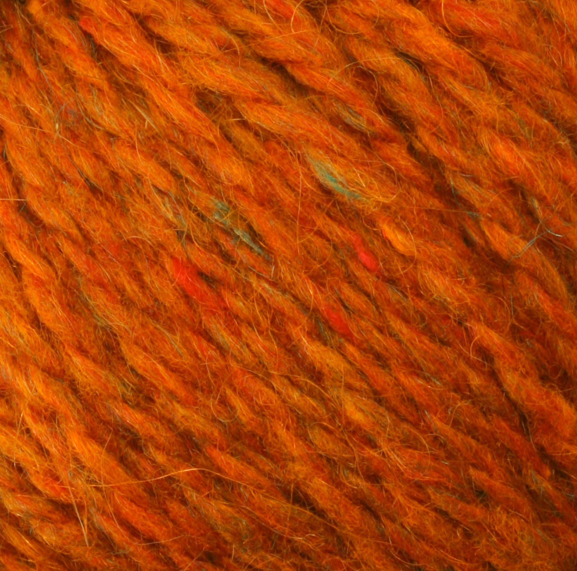 Close-up image of thick, orange Peace Fleece Yarn by Harrisville Designs with speckles of red and blue. The wool and mohair blend fibers are twisted together, showcasing a textured and cozy appearance suitable for knitting or crocheting projects.