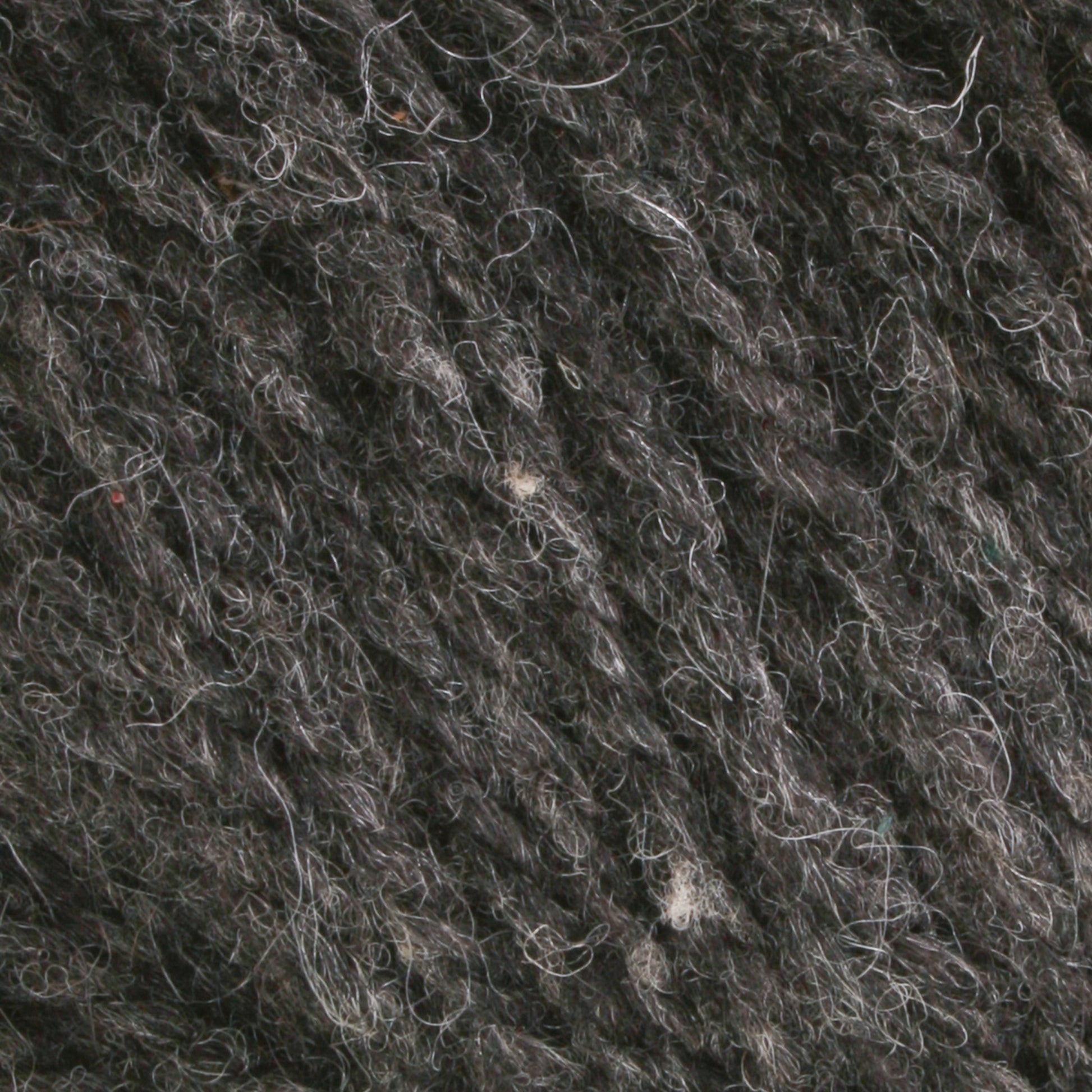 Close-up view of Bartlettyarns Maine Wool Yarn, a worsted weight yarn in heathered colors. The dark gray wool showcases various shades of gray intertwined, displaying a coarse and textured surface with visible fibers and strands.