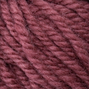 Close-up of thick, soft yarn in a warm, dusty rose color. The slightly fuzzy *Halcyon Yarn Classic Rug Wool* from *Caledonian Dye Works* showcases tightly twisted fibers clearly. This hand-dyed creation captures the intricate details of the strands and their gentle, plush appearance—a weaver's dream material.
