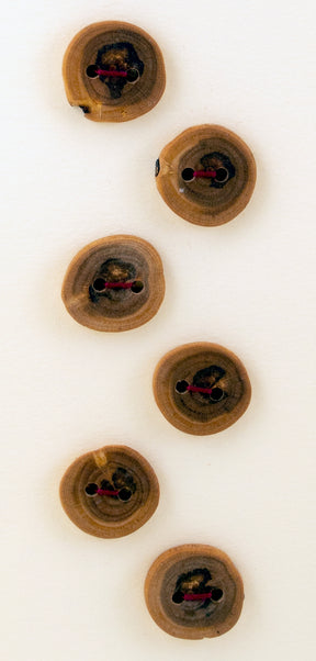 Six Buttons by Favour Valley Woodworking are round and crafted from locally sourced wood, each featuring unique grain patterns. The buttons have two holes each, with some holes threaded with dark strings. They are displayed in a loose vertical line against a light background.