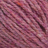 Close-up image of Harrisville Designs' Harrisville Highland - Cones in pink wool yarn, showcasing a beautiful range of shades from light to dark pink, interspersed with hints of orange and white fibers. The unscoured texture reveals the strands twisted together with spinning oils, giving it a soft and cozy appearance.