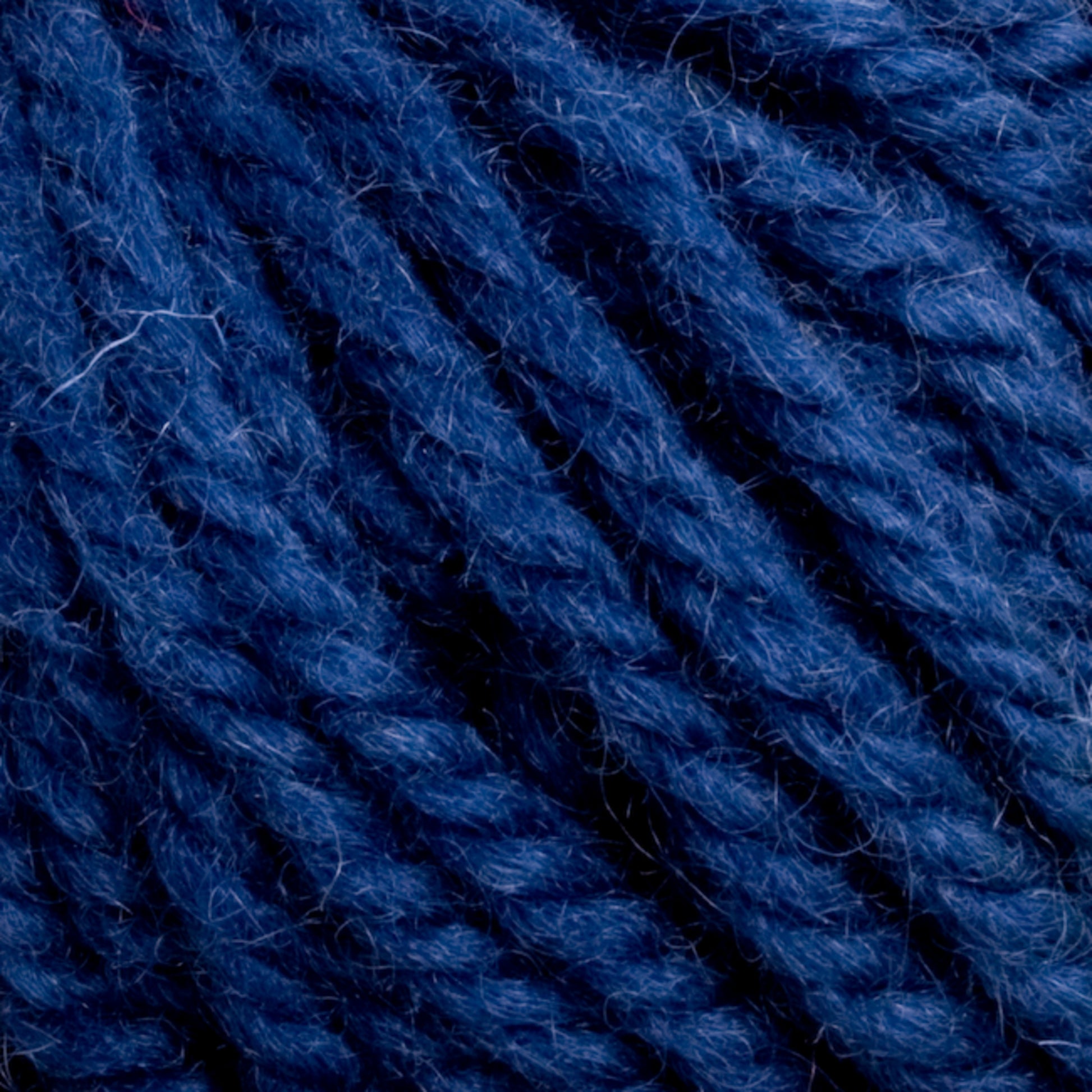 Close-up image of tightly woven blue yarn strands. The yarn, resembling Halcyon Yarn Classic Rug Wool by Caledonian Dye Works, exhibits a rich cobalt hue with subtle tonal variations, clearly showcasing the texture and twist of individual fibers. The image captures the intricate details and slight fuzziness of the fibers, making it perfect for rug weavers.