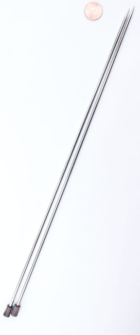 Two long, thin Accessories Unlimited Nova Platina Single Point Knitting Needles are placed parallel to each other on a white surface, with their pointy ends facing upward. A penny is positioned near the top right, providing a sense of scale for these straight needles. The knitting needles have small caps on their ends.