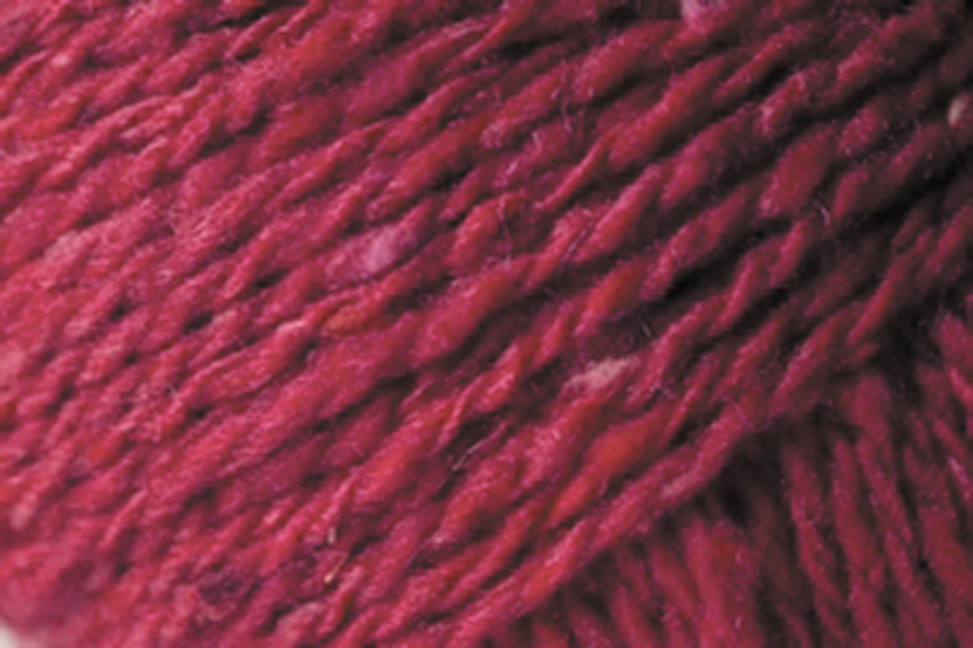 Close-up image of thick, twisted red fibers in a Jo Sharp Silkroad DK Tweed blend by Kingfisher Yarn & Fibre. The texture showcases various shades of red, giving it a rich and varied appearance. The fibers appear soft and dense, capturing the luxury of wool, silk, and cashmere.