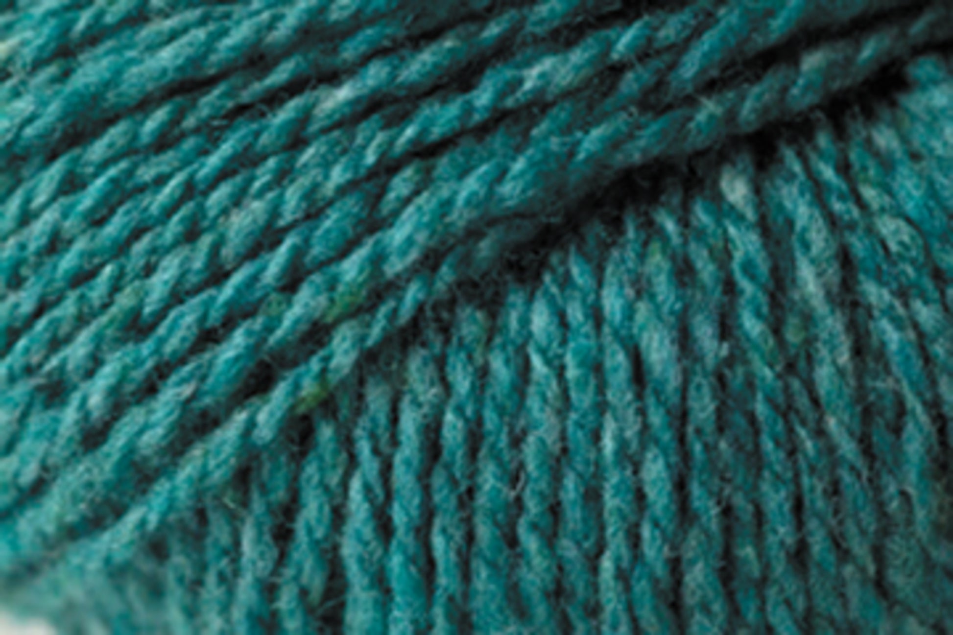 Close-up image of Jo Sharp Silkroad DK Tweed by Kingfisher Yarn & Fibre, showcasing its teal-colored, textured DK weight yarn with a soft, slightly fuzzy texture and tightly twisted strands. The yarn exudes luxury with its blend of wool and silk, featuring subtle variations in color that include hints of blue and green.