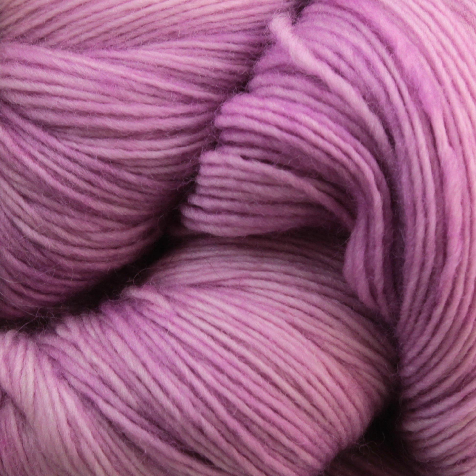 Close-up of soft, thin strands of Malabrigo Lace yarn in varying shades of pink and purple from Malabrigo Yarn, gently twisted together. The texture is smooth with fine lines visible, highlighting the delicate fibers and gradient colors, ideal for creating knitted shawls.