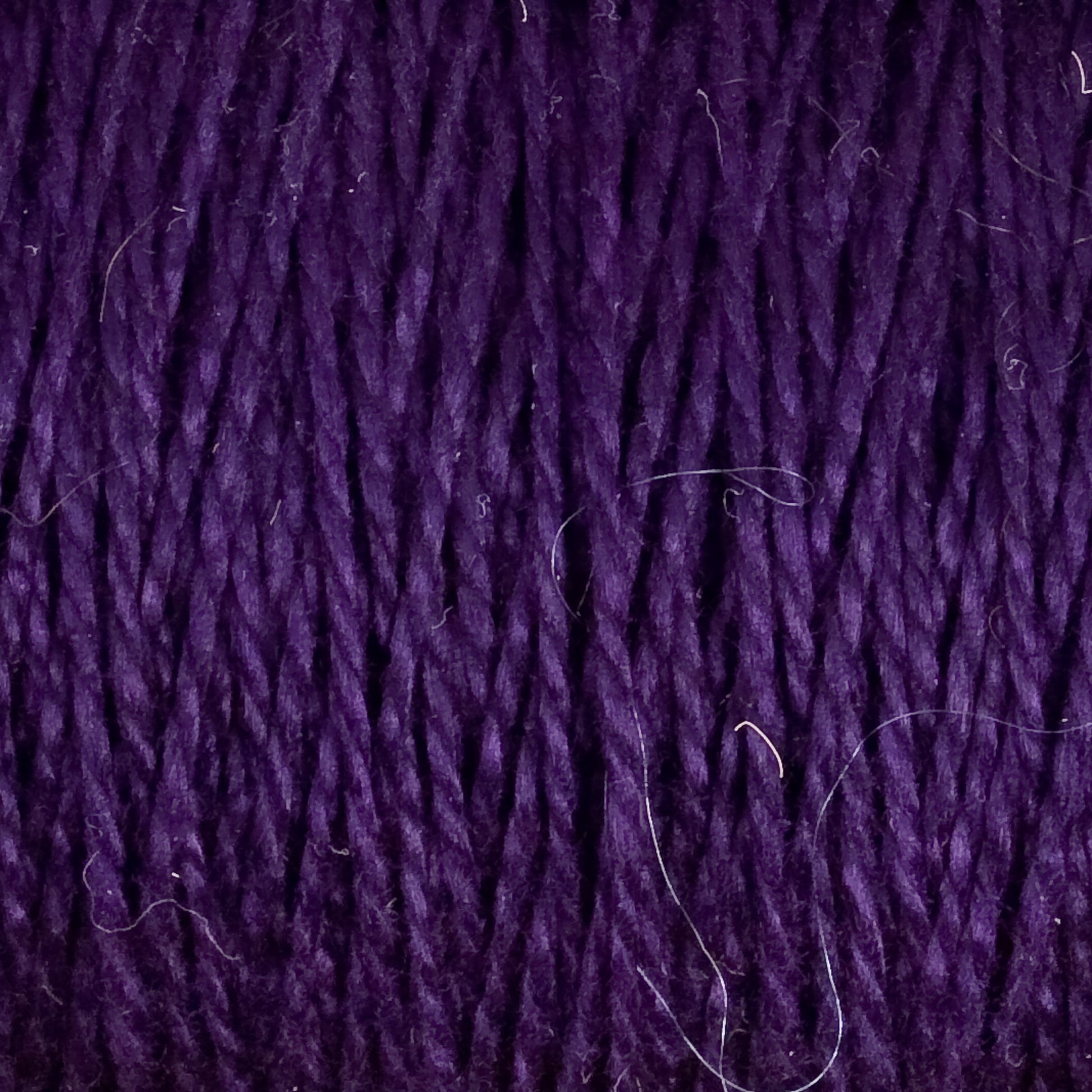 Close-up of dark purple, versatile 10/2 Pearl Cotton Yarn | Mini-cone by Supreme Corp. with a textured, intertwined appearance. The fibers appear soft and slightly fuzzy, with some stray threads visible against the deep purple backdrop. This yarn ensures colorfastness and adds a rich hue to any project.