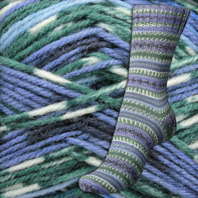 A single knitted sock crafted from Regia 4-ply Design Line by Arne & Carlos is displayed on a background made of thick, multi-colored yarn in shades of teal, blue, and white. The intricate pattern of the self-pattern sock yarn stands out against the textured yarn backdrop from Sirdar - Regia, Schachenmayr & Rowan.