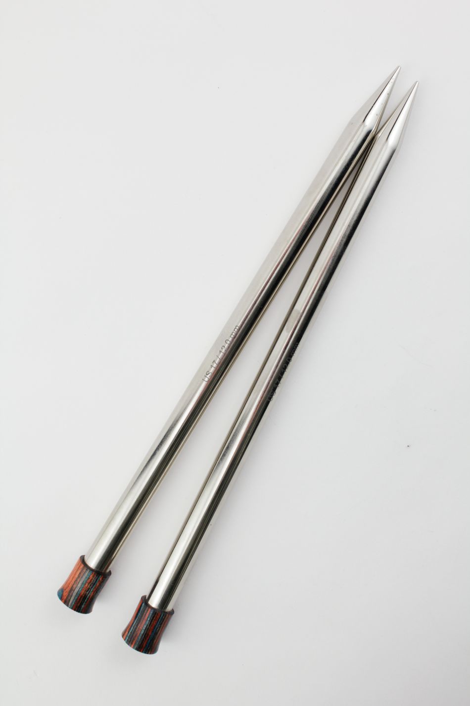 Two long, metal knitting needles with pointed tips are crossed at one end, resembling thin hollow brass pipes, and rest on a white background. The opposite ends feature small, colorful wooden caps. These Nova Platina Single Point Knitting Needles by Accessories Unlimited could be ideal for any Knitter's Pride collection.