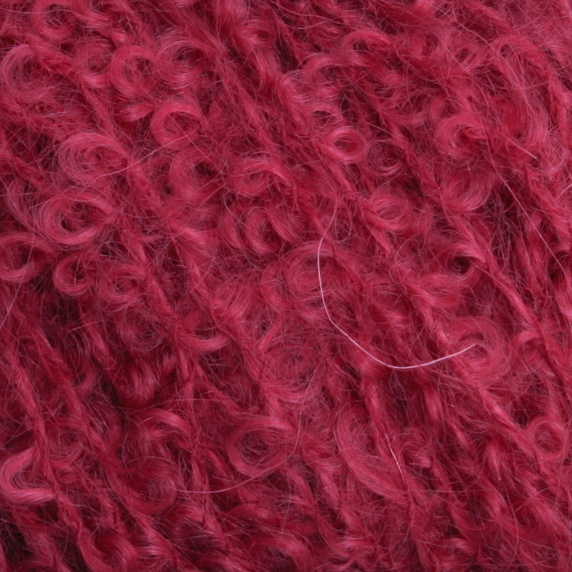 Close-up image of Caledonian Dye Works' vibrant red Victorian Bouclé Mohair Yarn. The texture appears soft and fluffy, with intricate loops and swirls intertwined, reminiscent of Halcyon's Signature Victorian Collection.