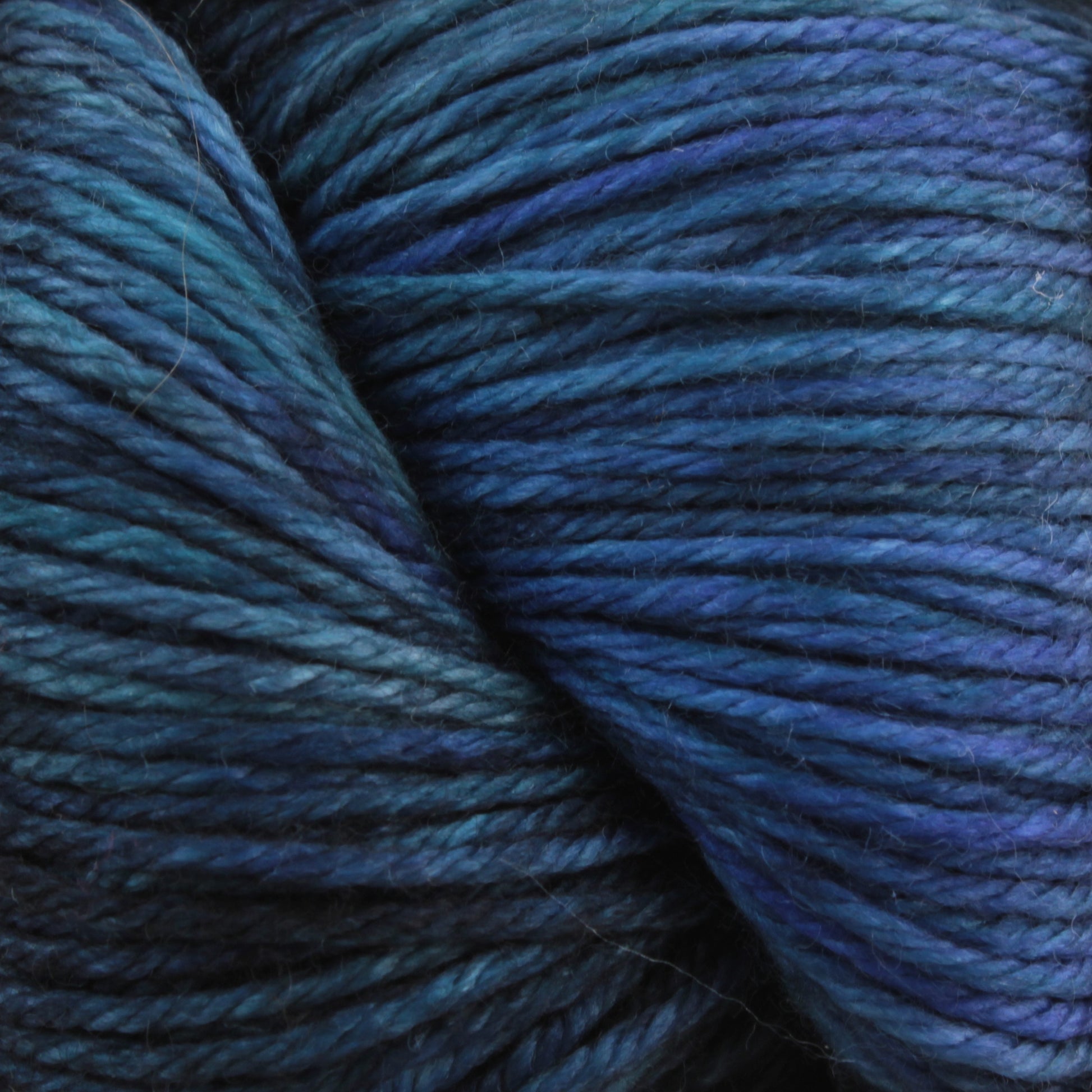 A close-up view of a skein of Malabrigo Yarn's Malabrigo Arroyo yarn showcases a stunning array of blue and teal hues. The tightly wound sport weight strands, made from superwash merino wool, highlight the rich and vibrant colors in exquisite detail, making it perfect for lightweight garments.