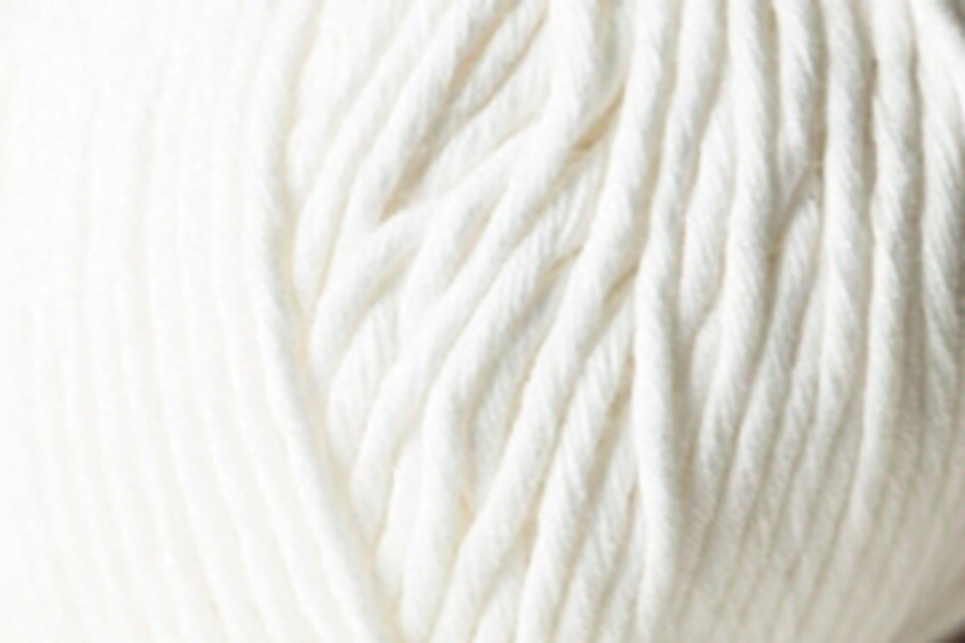 A close-up image of the Jo Sharp Desert Garden Aran Cotton from Kingfisher Yarn & Fibre highlights the soft, white yarn, revealing the texture and twists of its fibers. The thick, fluffy yarn suggests it is an Aran weight cotton suitable for knitting or crocheting warm, cozy items. The background is entirely filled with the yarn, emphasizing its texture and knitting performance.