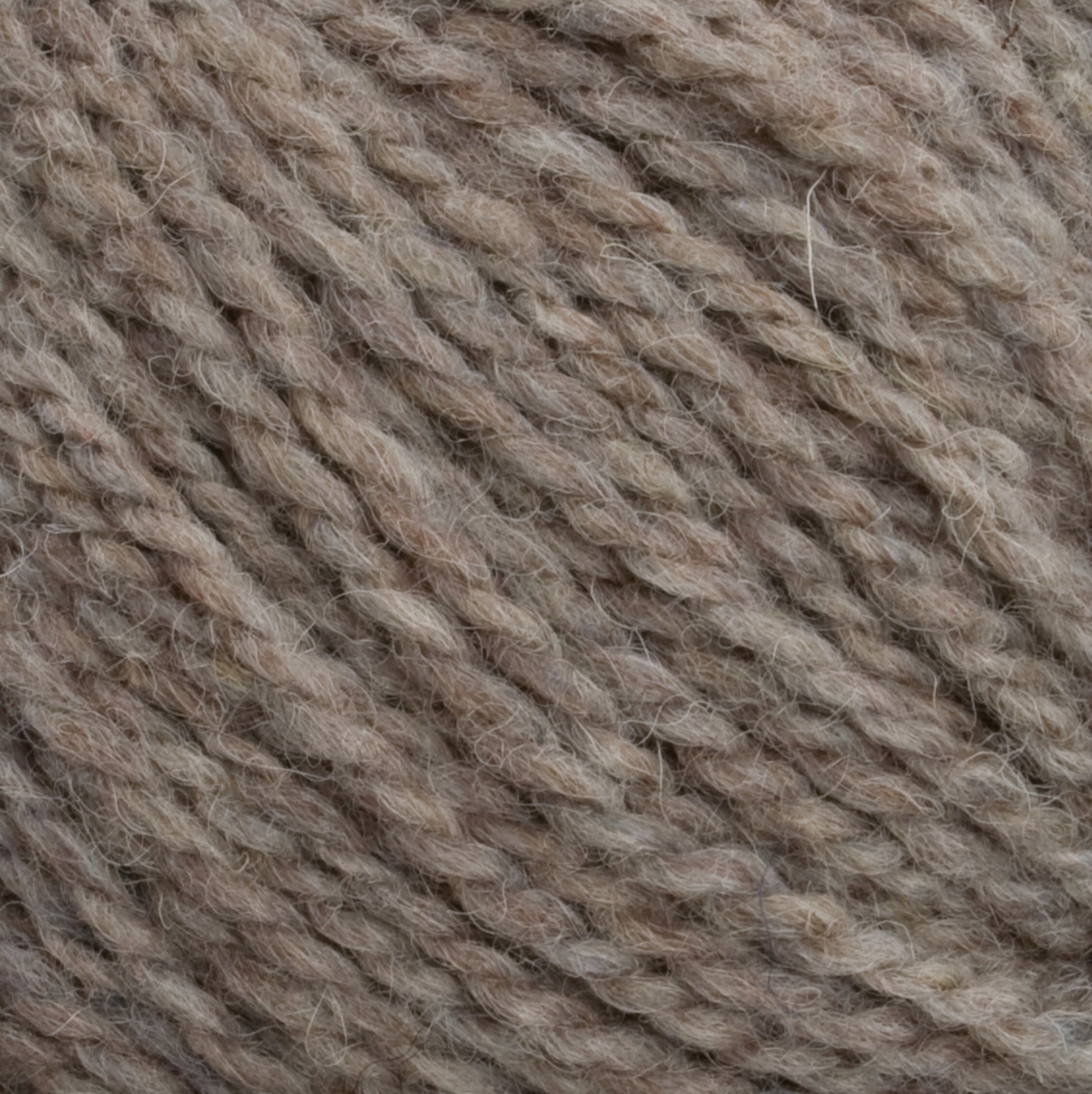 Close-up of Harrisville Designs Harrisville Shetland Yarn - Unwashed Cones in a beige hue, highlighting its twisted fibers and soft texture. The yarn appears thick and slightly hairy, suggesting it is crafted from natural fibers such as wool. The color showcases subtle variations within the beige spectrum, making it an ideal choice for Fair Isle knitting designs.