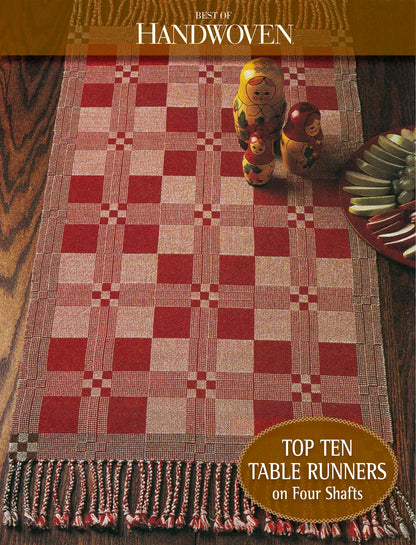 A handwoven table runner featuring a red and beige checkered pattern is laid gracefully on a wooden table. Three Russian nesting dolls and a stack of vibrant, colorful plates adorn the table. A text overlay reads "Best of Handwoven" and "Top Ten Table Runners on Four Shaft Loom," highlighting the acclaimed printed version by Long Thread Media.