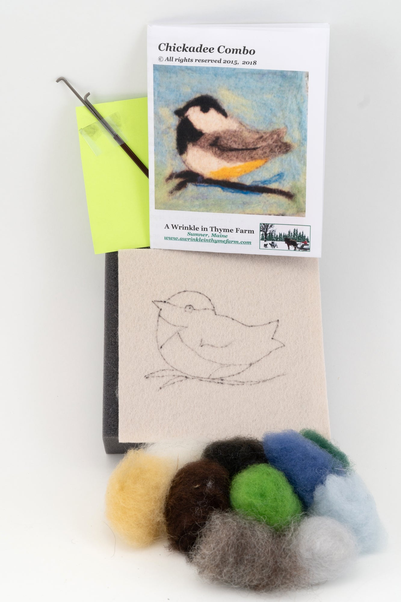 The Thyme Tile Felting Kit by A Wrinkle in Thyme Farm is shown, featuring a booklet with an image of a chickadee, a felting needle, and various colored wool roving. An outline of a chickadee is drawn on a piece of wool felt for reference.