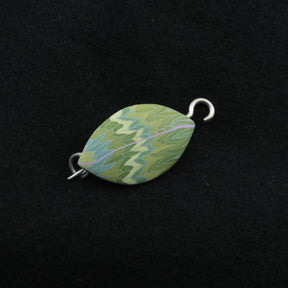 The Leaf Shawl Pin by Bonnie Bishoff Designs is an exquisite marquise-shaped piece featuring a vibrant, intricate polymer clay design in shades of green, blue, and yellow. Both ends have metal loops, indicating its use as a jewelry clasp or shawl closure. The design stands out beautifully against a black background.