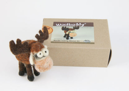 A needle-felted moose figurine stands next to a cardboard box labeled "Woolbuddy Needle Felting Kits." The box, from the Woolbuddy brand, features an image of the same moose and indicates the kit size is medium. Complete with wool roving and felting needles, this kit allows you to create a moose with exaggerated eyes and antlers.