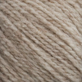 Close-up view of Harrisville Shetland Yarn - Unwashed Cones by Harrisville Designs, showcasing intermixed light beige and off-white fibers. The yarn has a soft and fluffy appearance with visible individual threads tightly twisted together, creating a variegated pattern perfect for crafting Fair Isle knitting designs.