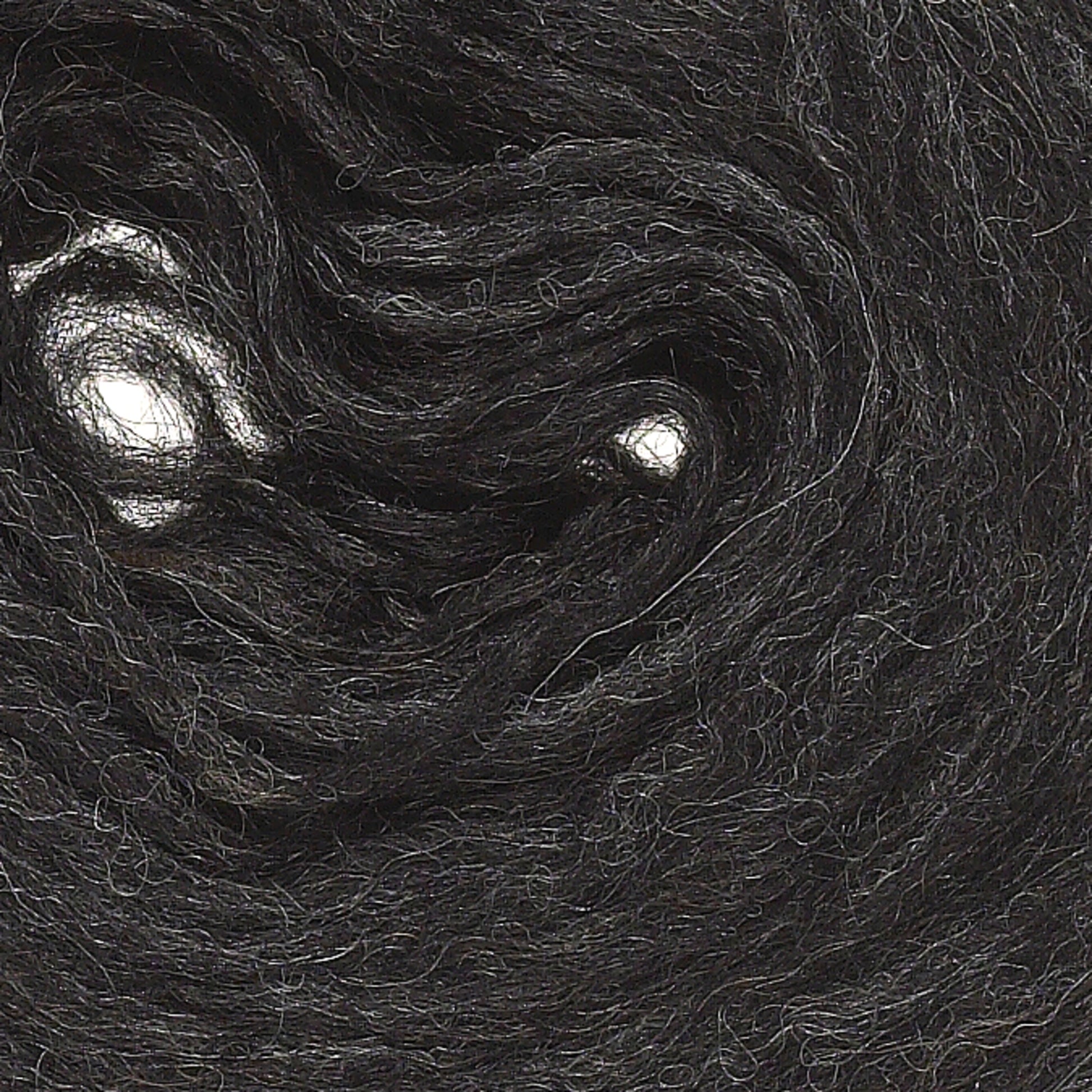 A close-up view of dark, thick Plötulopi Unspun Icelandic Wool Yarn by Berroco, Inc., intricately wound in a circular pattern. The fibers are slightly frizzy, with some light reflections creating a swirl effect in the yarn. The texture appears soft and fuzzy.