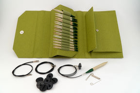 A green fabric case from the Lykke Interchangeable Circular Bamboo Knitting Needle Set, 5" by Knitting Fever / Euro Yarns is open to display wooden bamboo knitting needles with green caps. In front of the case lie three circular knitting cables, several black cable stoppers, and a green-handled tool. This interchangeable knitting set also includes additional small metal parts for convenience.