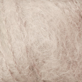 Close-up of a ball of Victorian Brushed Mohair Yarn by Caledonian Dye Works, featuring light beige, fuzzy fibers with an airy texture. The mohair appears soft and wispy, creating a delicate and textured surface. This luxurious yarn has a neutral, slightly warm color that exudes an elegant charm.