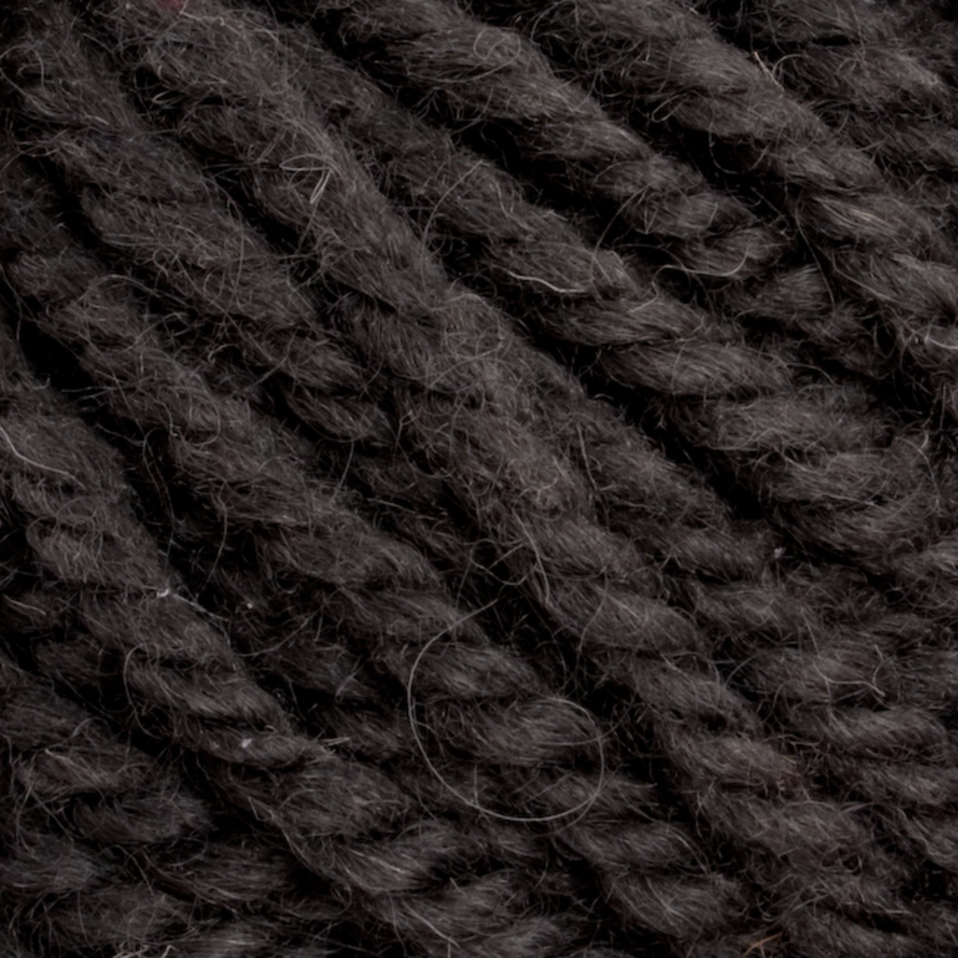 Close-up of dark, thick strands of Halcyon Yarn Classic Rug Wool | Skein by Caledonian Dye Works, tightly twisted together with a slightly fuzzy texture. The yarn appears to be made of a natural material, possibly hand-dyed wool favored by weavers, and has a dark grayish-black color.