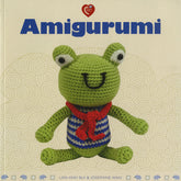 The book cover for "Amigurumi" by Ingram Content features a charming crocheted stuffed toy—a green frog with bulging eyes, wearing a red scarf and a blue and white striped shirt. The background is a light beige color adorned with swirling patterns, and the authors Lan-Anh Bui & Josephine Wan are listed at the bottom.