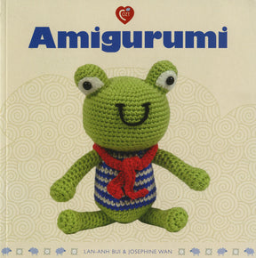 The book cover for "Amigurumi" by Ingram Content features a charming crocheted stuffed toy—a green frog with bulging eyes, wearing a red scarf and a blue and white striped shirt. The background is a light beige color adorned with swirling patterns, and the authors Lan-Anh Bui & Josephine Wan are listed at the bottom.