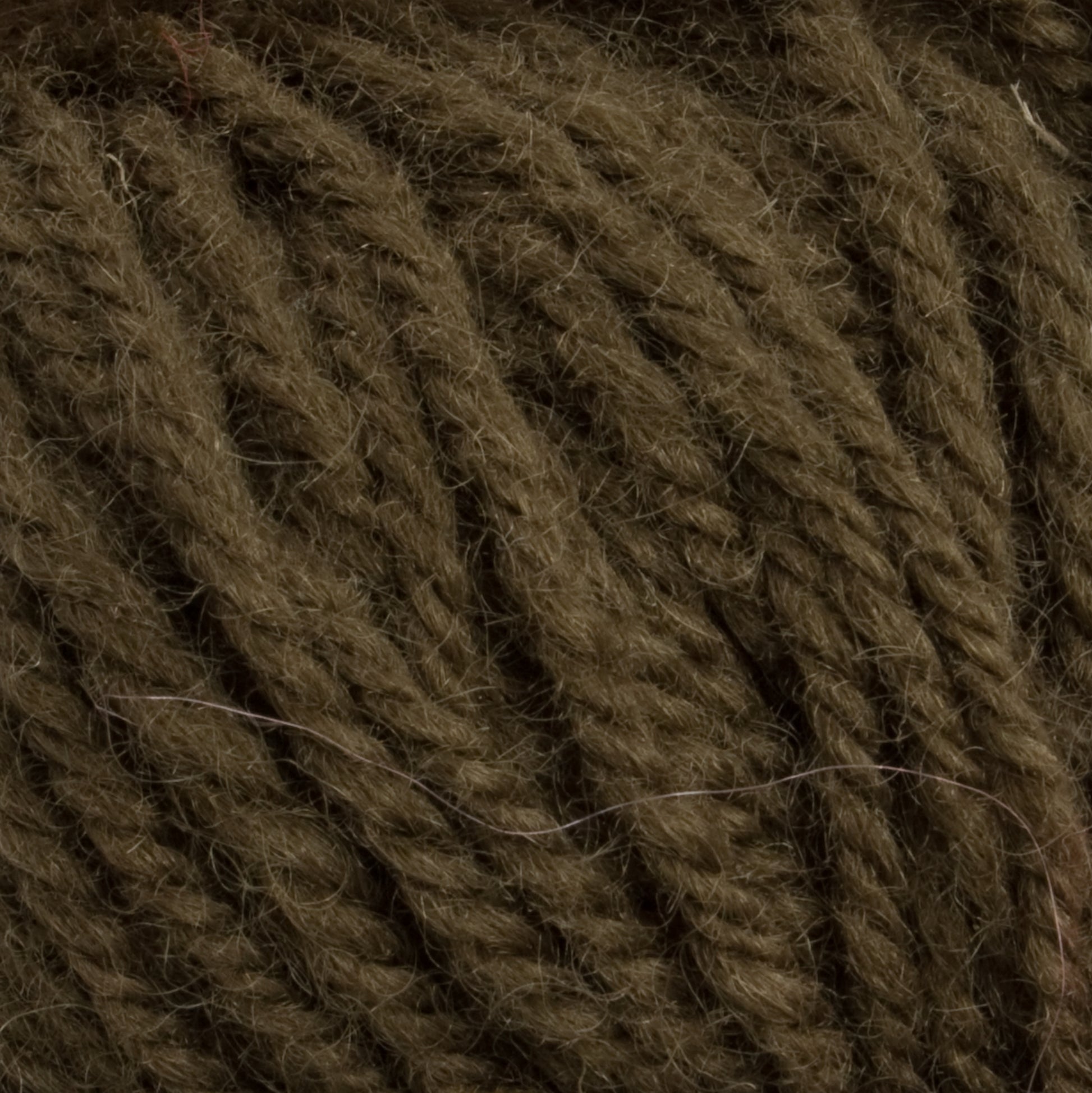 A close-up view of the dark brown Halcyon Deco Rug Wool by Caledonian Dye Works, showcasing its soft and fuzzy texture with thick, twisted fibers running parallel to one another. The 100% wool yarn appears dense and slightly coarse, ideal for knitting or crocheting warm garments and accessories.