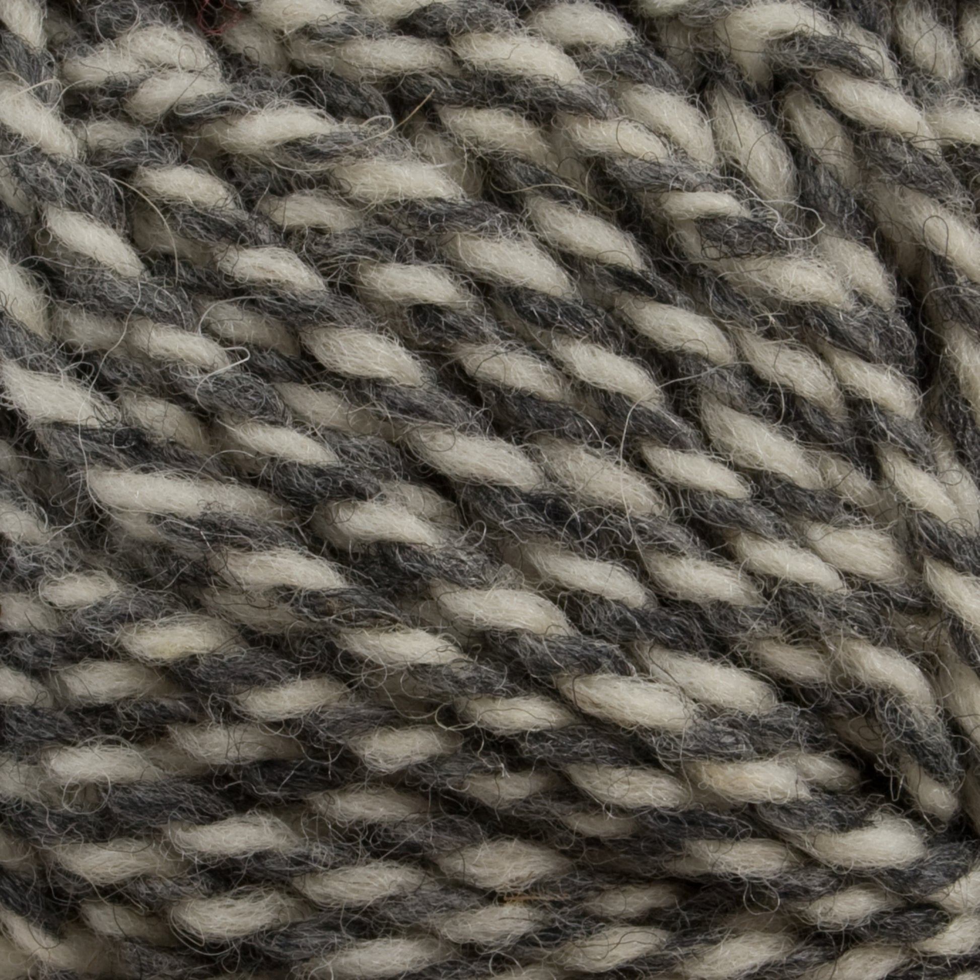 Close-up image of Tuffy Canadian Sock Yarn, a worsted weight yarn from Briggs & Little, showcasing interwoven strands of cream and dark gray fibers that create a marbled effect. Ideal for cozy winter socks, the texture appears soft and slightly fuzzy.