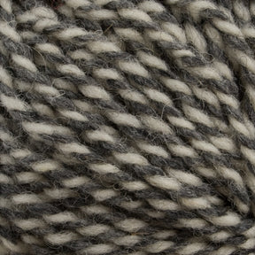 Close-up image of Tuffy Canadian Sock Yarn, a worsted weight yarn from Briggs & Little, showcasing interwoven strands of cream and dark gray fibers that create a marbled effect. Ideal for cozy winter socks, the texture appears soft and slightly fuzzy.