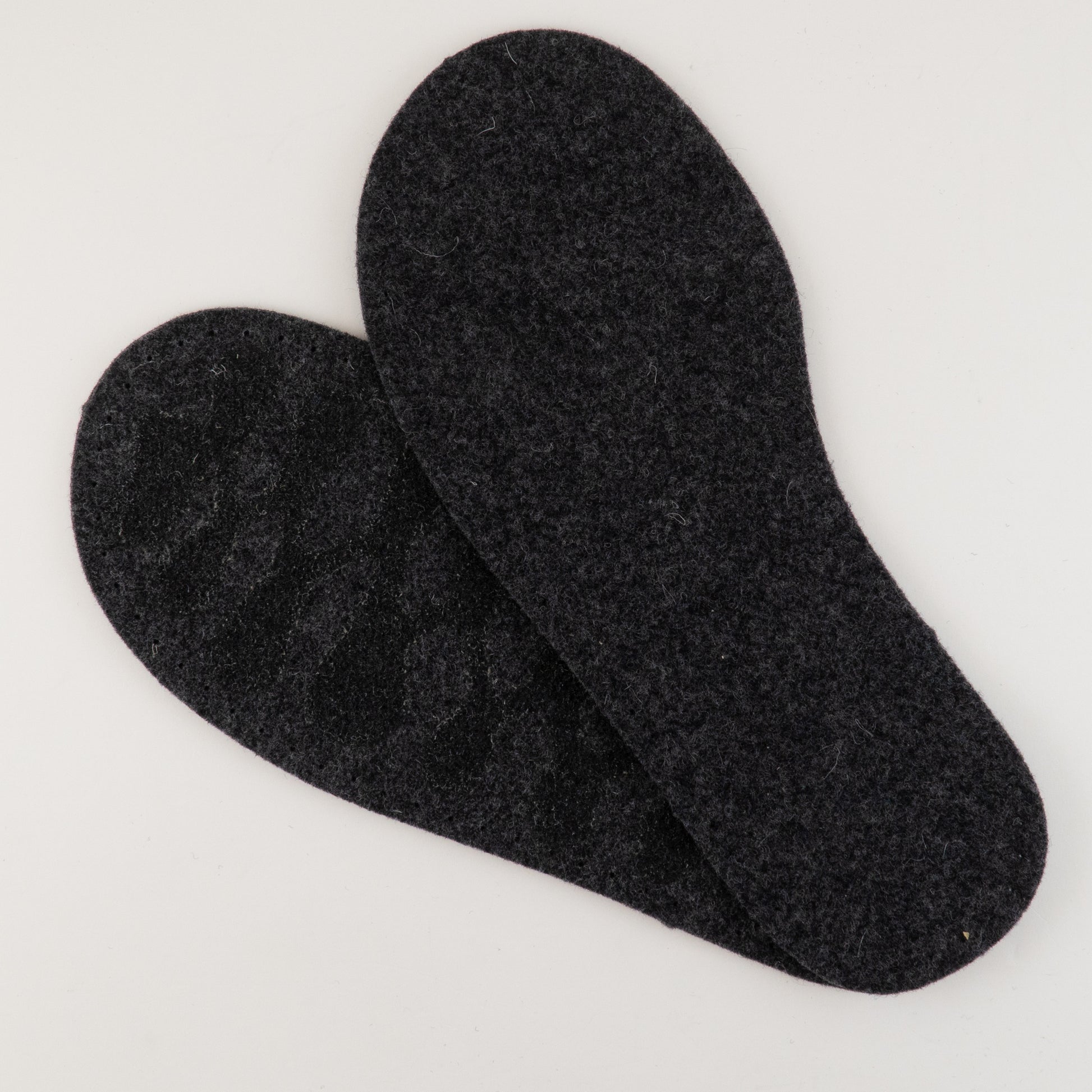 A pair of Adult's Thick Felt Slipper Soles w/Latex Grip by Joe's Toes are placed overlapping each other on a white background, with one insole slightly on top of the other. Made from eco-friendly wool, they appear to be designed for use in shoes for added comfort and warmth.