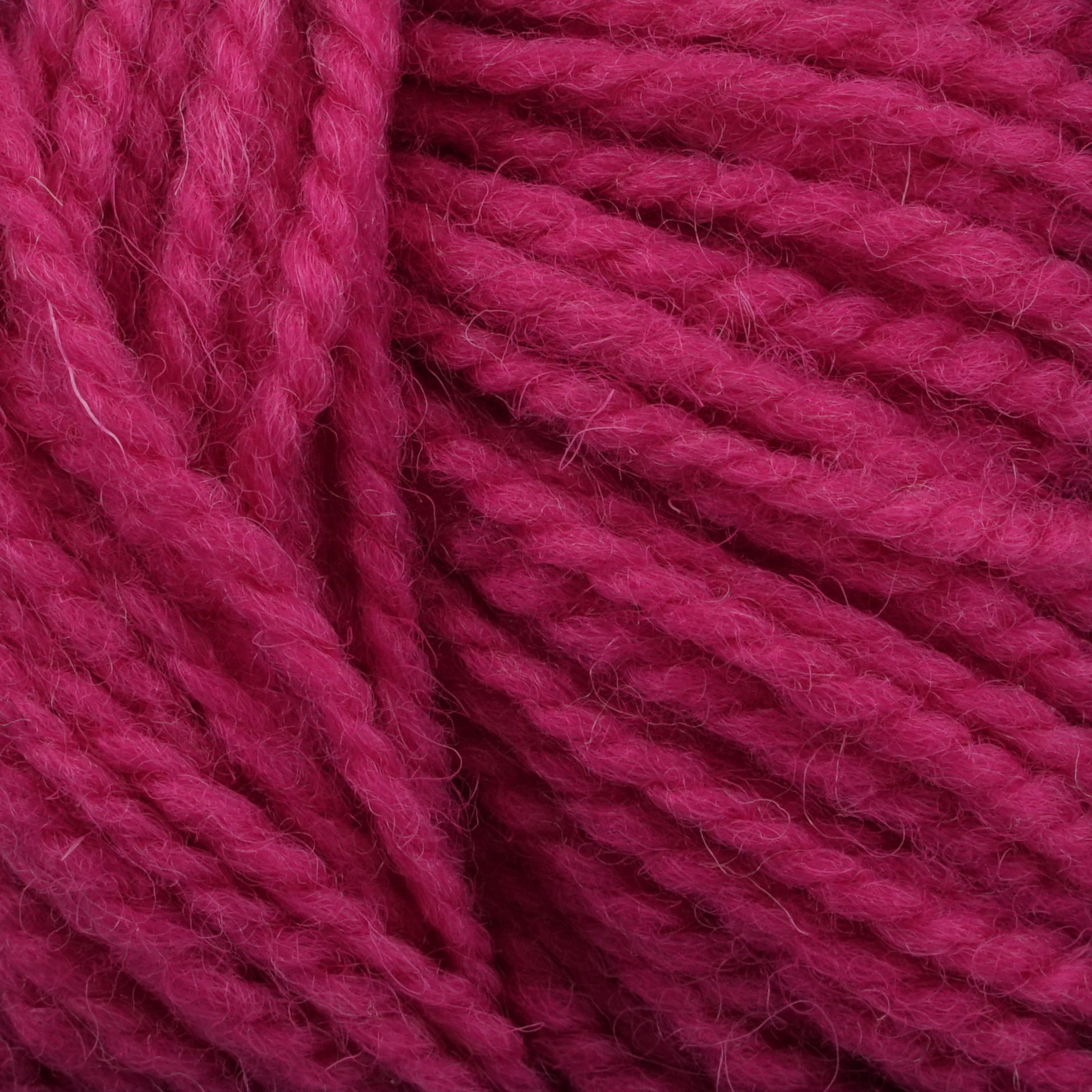 Close-up of dense, soft red yarn fibers intertwined together. The texture appears plush and thick, perfect for knitting or crocheting projects like winter socks. Made from Tuffy Canadian Sock Yarn by Briggs & Little in worsted weight yarn, the deep, rich shade of red gives a warm and cozy feeling.