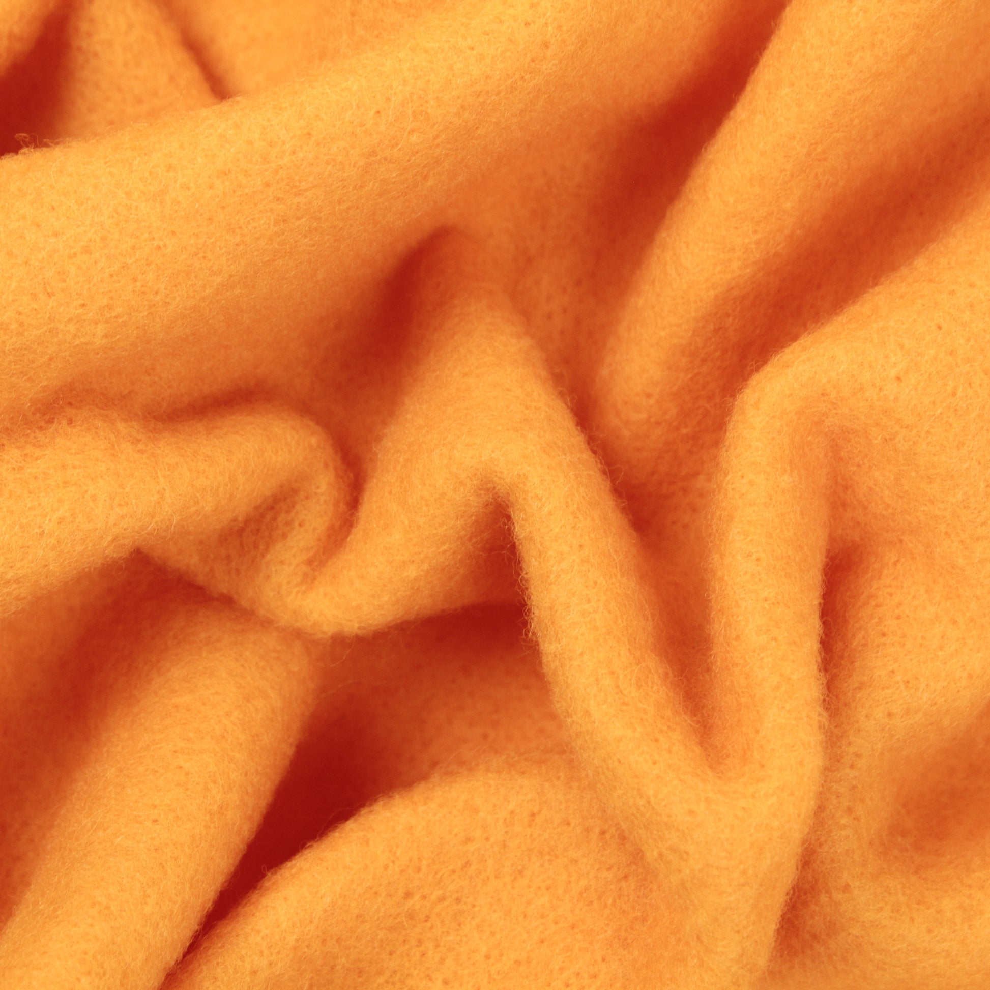 Close-up of the soft, orange Europa Wools Ltd Merino Prefelt with a slightly fuzzy texture. The fabric is loosely gathered, creating gentle folds and creases. The vibrant and warm color makes it ideal for felting projects.