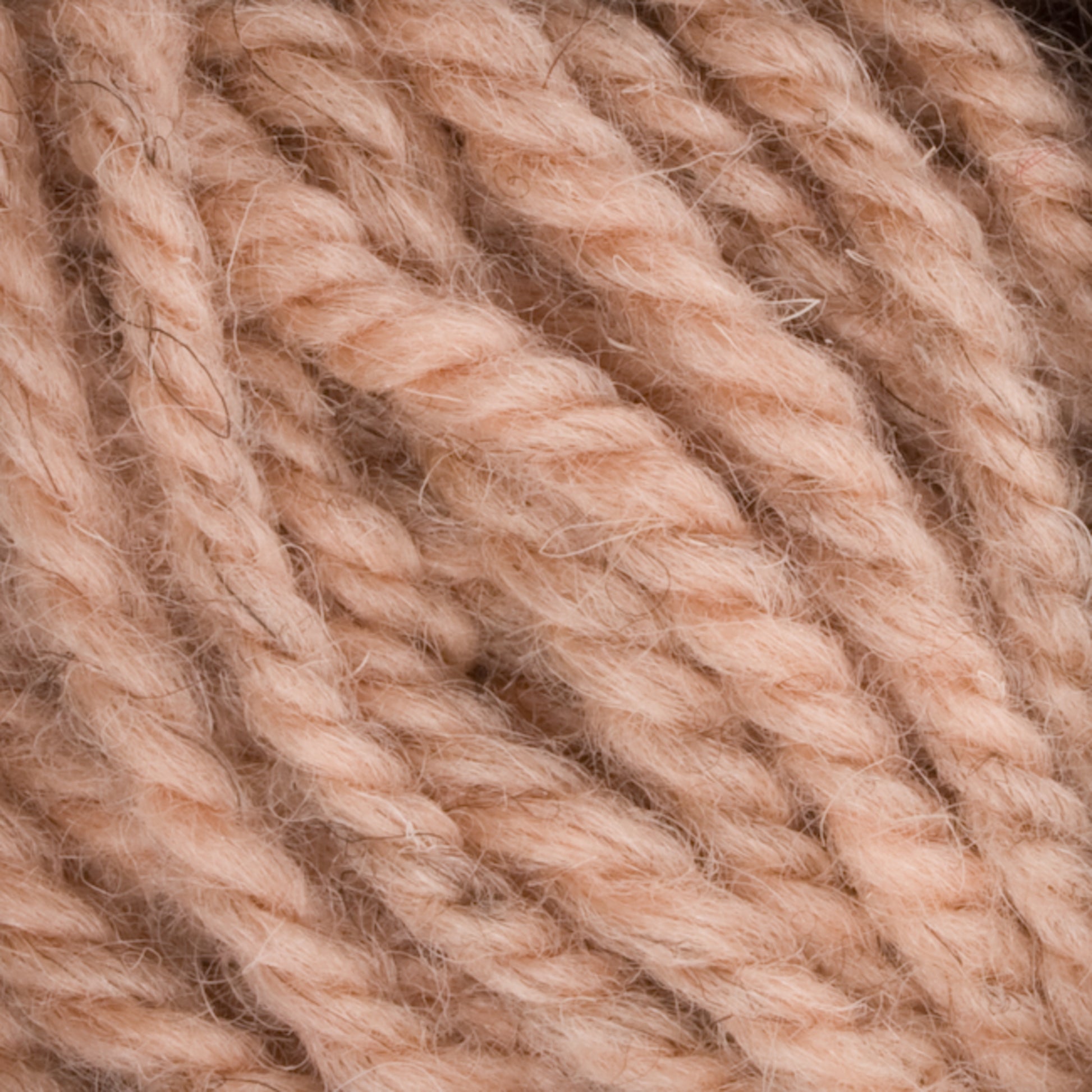 Close-up of soft, thick, beige yarn from Caledonian Dye Works' Halcyon Yarn Classic Rug Wool | Strand, showcasing its textured and twisted fibers. The yarn has a slightly fuzzy appearance and appears to be made of natural fibers, making it perfect for rug weavers seeking top-quality classic rug wool.