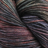 A close-up view of Malabrigo Sock yarn by Malabrigo Yarn, showcasing its variegated Merino wool in shades of dark green, red, blue, and purple, tightly wound into a skein that highlights the texture and kettle dyed multicolors.