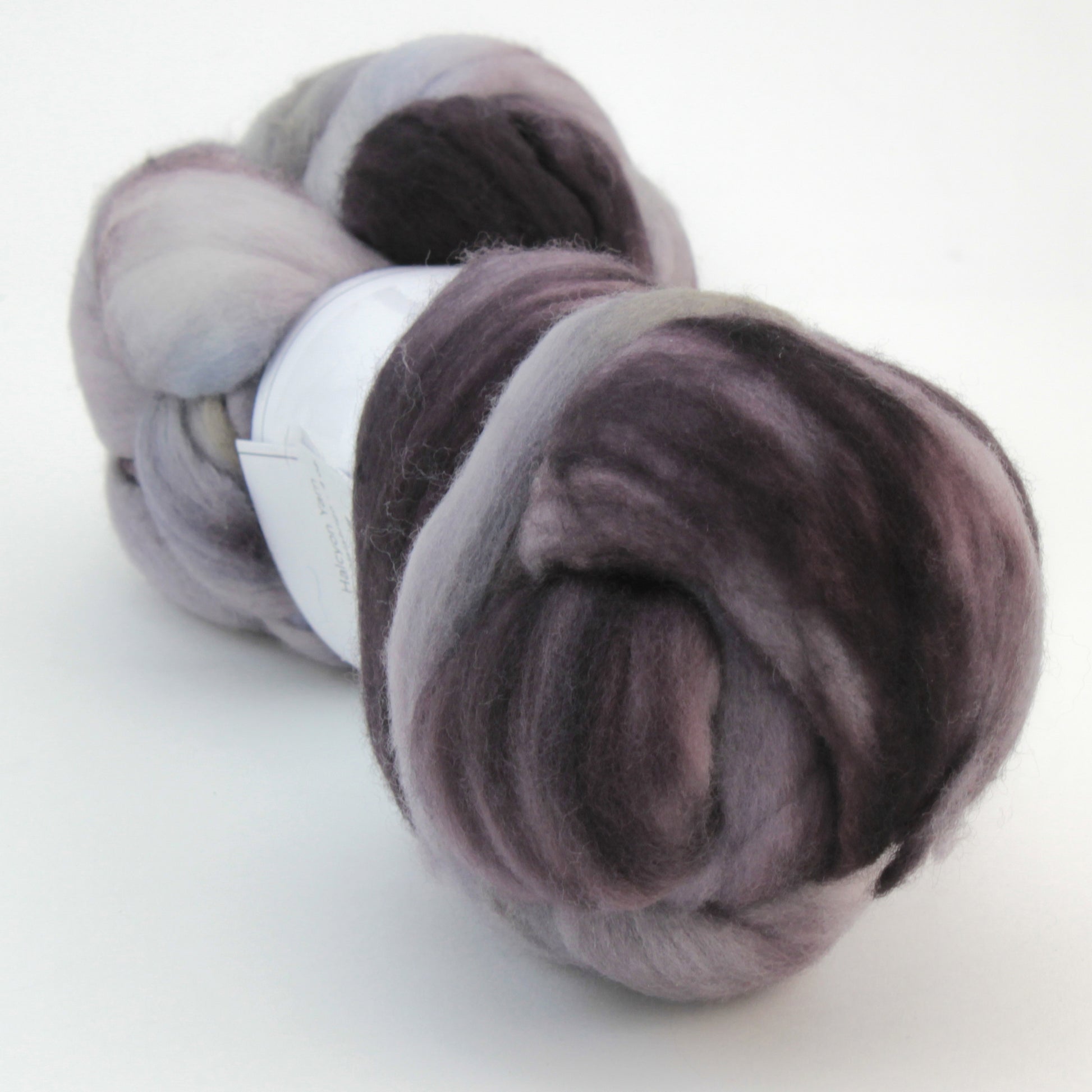 A skein of soft, hand-dyed Nube by Malabrigo in shades of grey, black, and white. The roving is loosely coiled and appears thick and fluffy, suitable for spinning into yarn or felting projects. Reminiscent of other offerings by Malabrigo Yarn, the overall texture looks smooth and woolly.