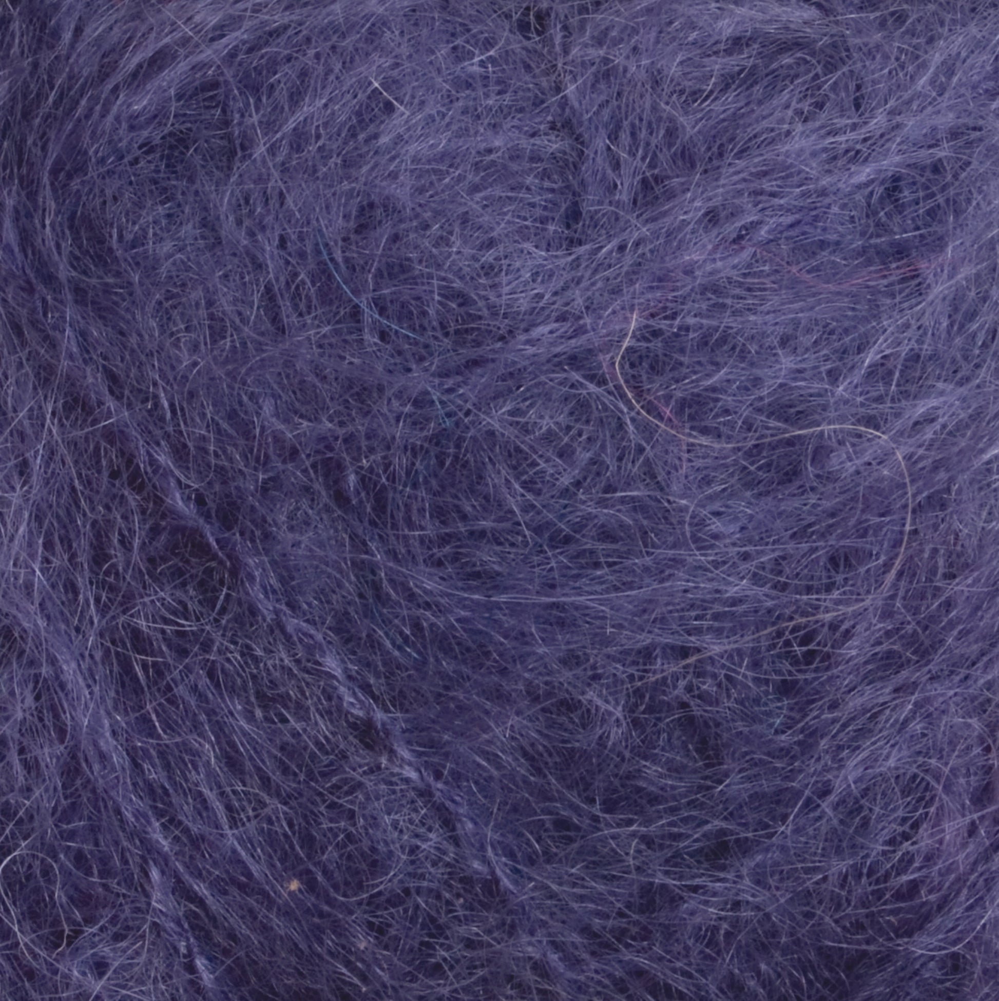 A close-up shot of Victorian Brushed Mohair Yarn by Caledonian Dye Works reveals a luxuriant texture featuring intertwined purple fibers, giving a fuzzy, hairy appearance. The chaotic and dense fibers create a slightly uneven surface with various shades of purple. This soft texture is reminiscent of luxurious mohair yarn or fabric, suggesting premium quality.