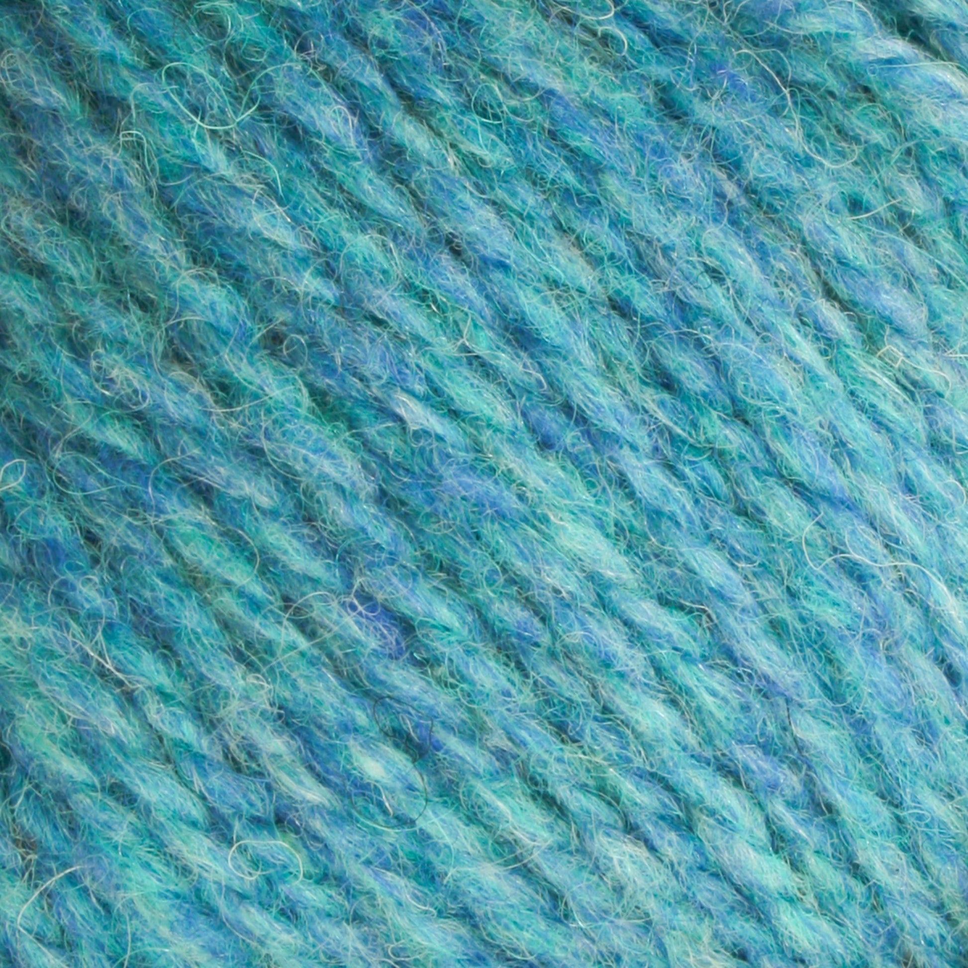 Close-up of Bartlettyarns Maine Wool Yarn in blue, showcasing its heathered colors with hints of green. The texture is soft and fibrous, blending tightly spun and fluffy strands. This worsted weight yarn from Bartlettyarns reveals the intricate twists and plies in the material.