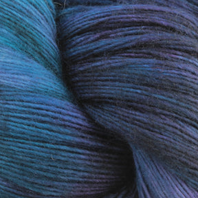 Close-up image of Malabrigo Yarn's Malabrigo Lace yarn, showcasing rich, transitioning colors from deep purple to vibrant blue. The texture of the merino wool strands is visible, highlighting the fibers and soft appearance, making it ideal for knitting or crocheting projects, especially intricate knitted shawls.