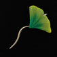 The Short Stick Shawl Pin by Bonnie Bishoff Designs from Bonnie Bishoff is a brooch designed to resemble a ginkgo leaf, featuring a twisted silver stem and a vibrant green and yellow gradient leaf adorned with delicate red vein lines set against a black background—perfect for lightweight shawl closures or adding flair to knit wearables.