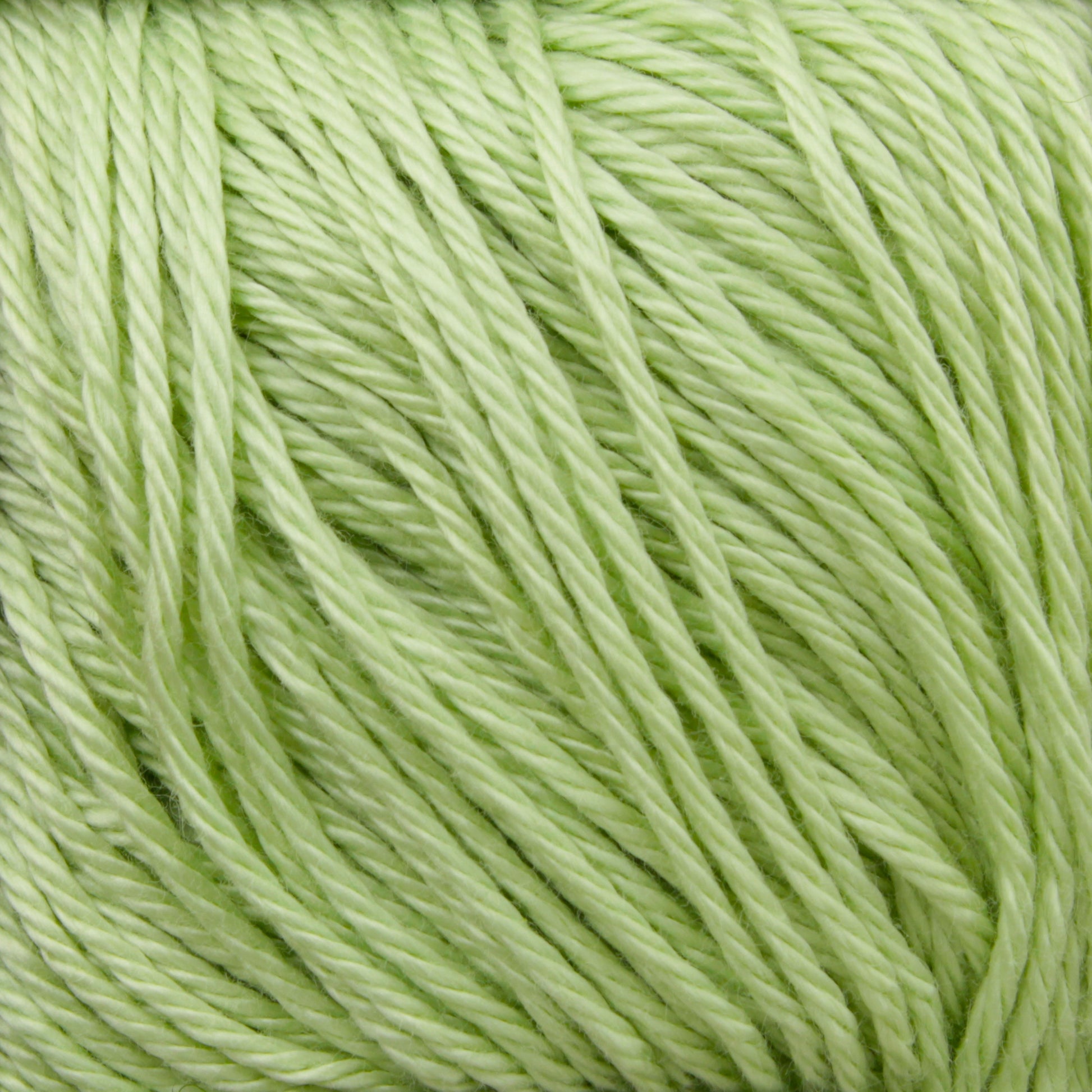 Close-up image of light green yarn strands tightly wound together, showcasing the texture, strands, and slight sheen of the Cascade Ultra Pima Cotton Yarn by Cascade Yarns. The color is a soft, pale green, giving a fresh and natural appearance. This yarn has a remarkably soft hand that adds to its appeal.