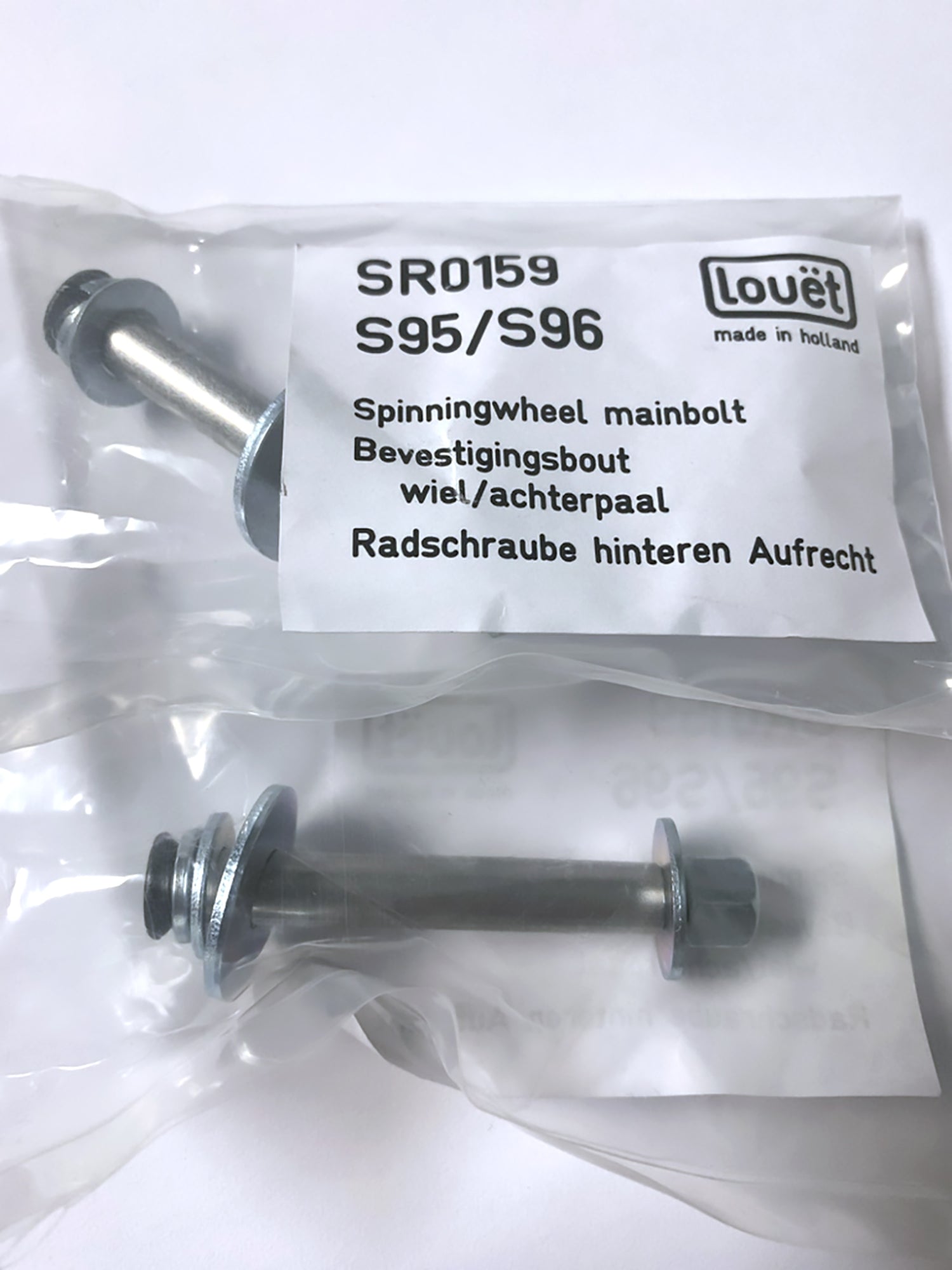 Close-up of two Louët Spinning Wheel Main Bolts in individual plastic bags with labels. The label includes the text "SR0159 S95/S96," "Louët Inc. made in Holland," and multiple translations for "Spinningwheel mainbolt" and "attachment bolt for rear upright/backpost.