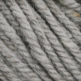 Close-up of several thick strands of light grey Halcyon Yarn Classic Rug Wool by Caledonian Dye Works, showcasing a textured, fibrous surface. The strands are tightly twisted together, giving a rugged and durable appearance. Subtle variations in the hand-dyed grey color contribute to a natural look.